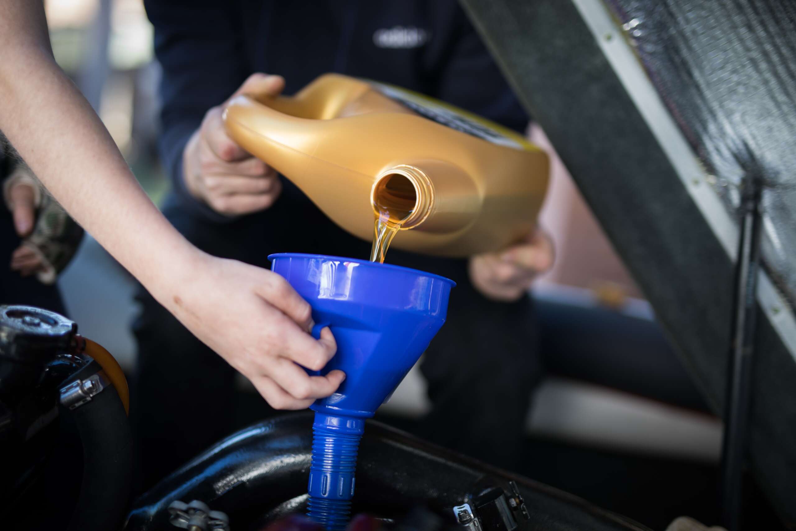 Person pouring engine oil into a blue funnel during an oil change service, emphasizing vehicle maintenance and care at Auto Star in Graham, WA.