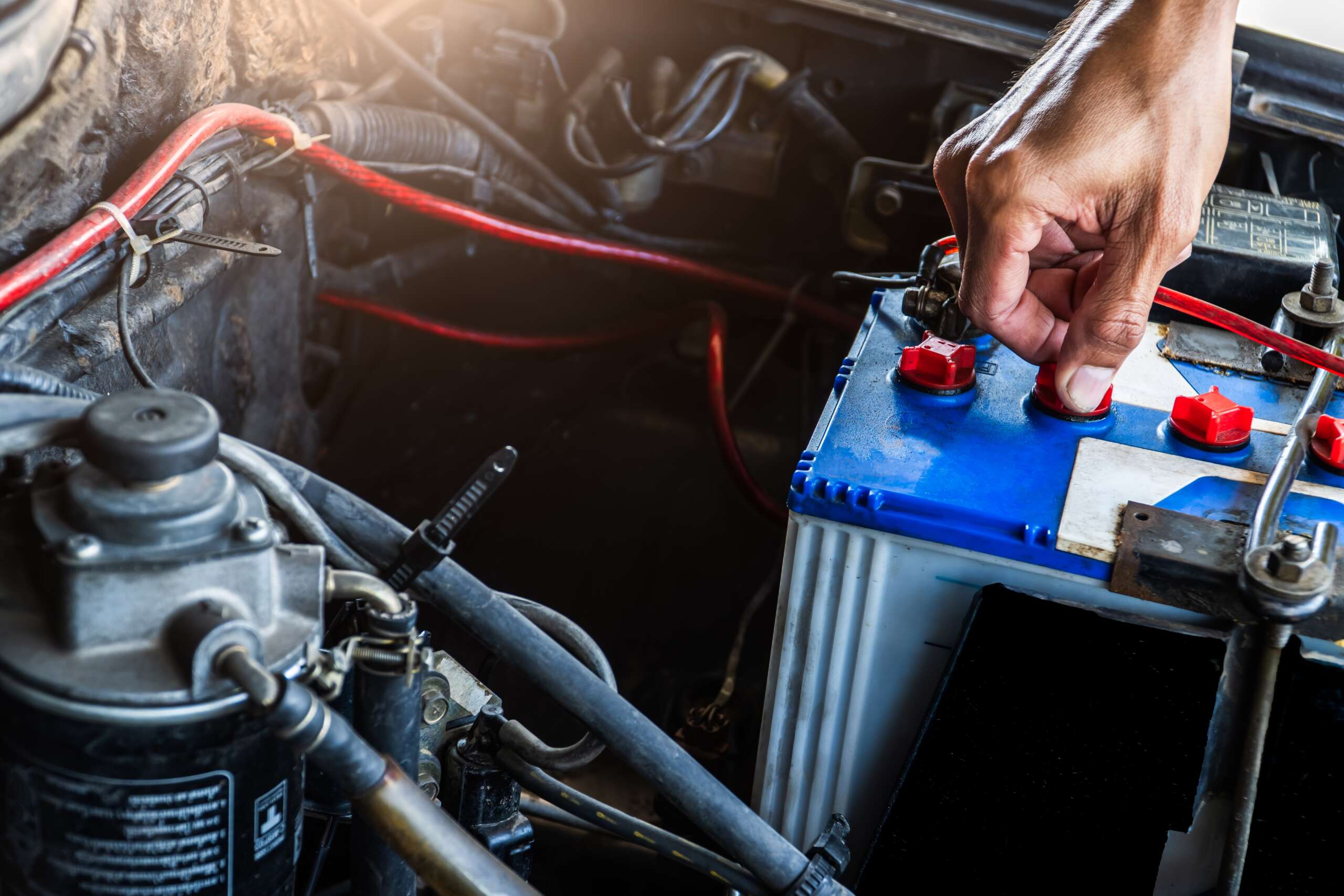 Hand inspecting car battery connections in an engine compartment, emphasizing vehicle maintenance and preventative care at Auto Star.