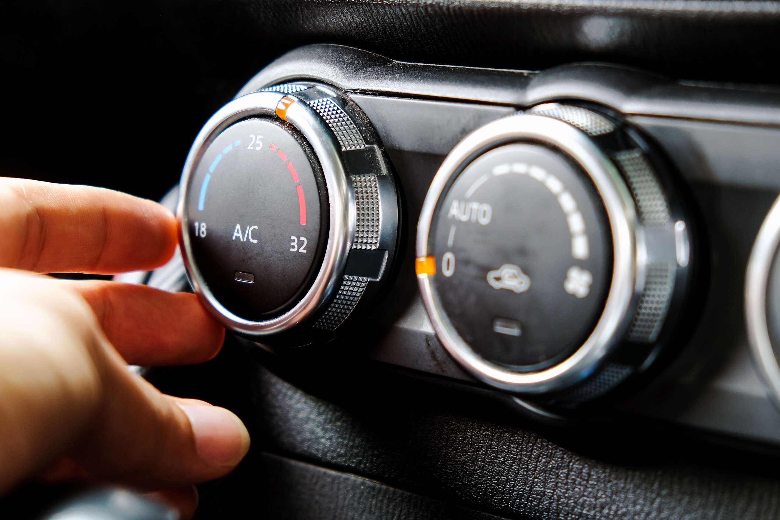 Close-up of a hand adjusting a car air conditioning control dial, displaying temperature settings and A/C function, relevant to vehicle heating and A/C repair services.