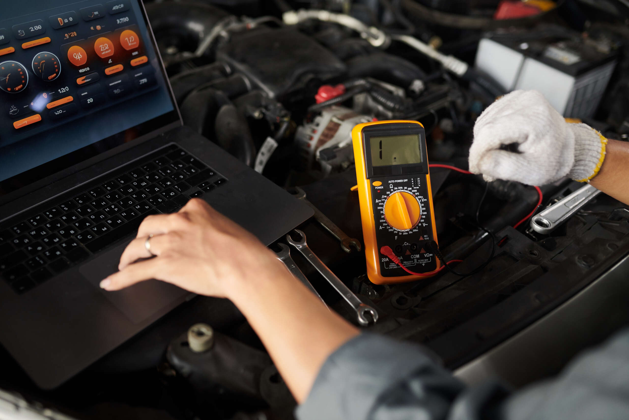 Mechanic using a multimeter and laptop for advanced car diagnostics in an auto repair setting.